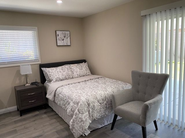 A cozy bedroom with a double bed, patterned bedding, a nightstand, and an armchair by the window.