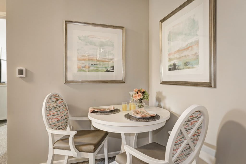 A cozy dining nook featuring a round table with two chairs, decorated with wall art and a small floral arrangement.