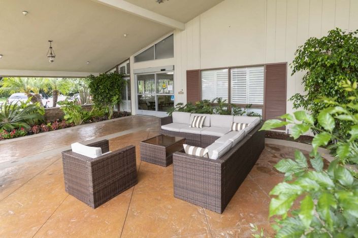 A modern outdoor patio with a comfortable seating arrangement, including a sofa set, armchair, and table surrounded by lush greenery.