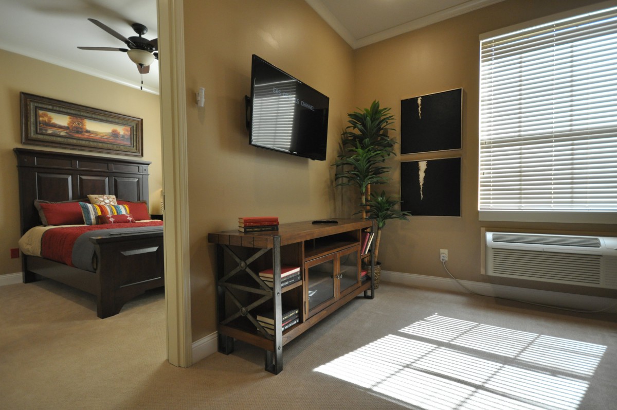 A cozy living room with a wall-mounted television and a wooden console, bathed in natural sunlight.