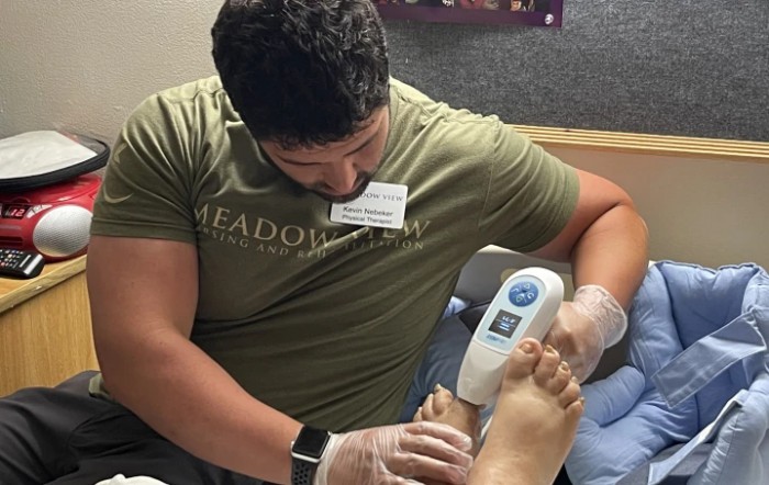 A healthcare professional examining a patient's foot using a handheld device in a clinical setting.