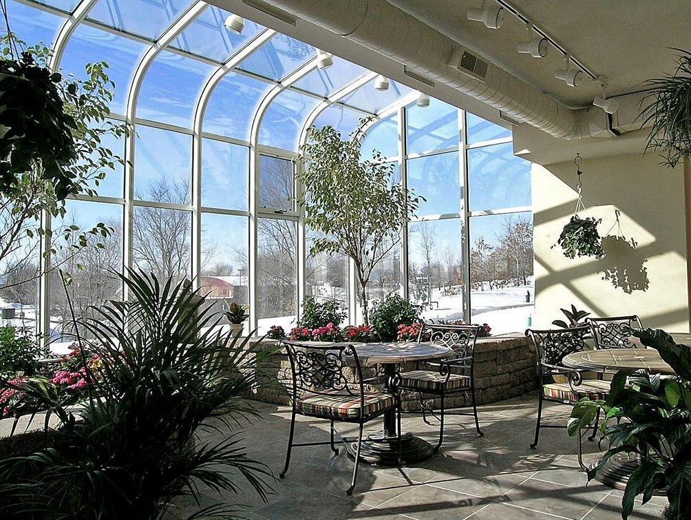 A sunny conservatory with glass ceilings, featuring lush plants and seating arrangements.