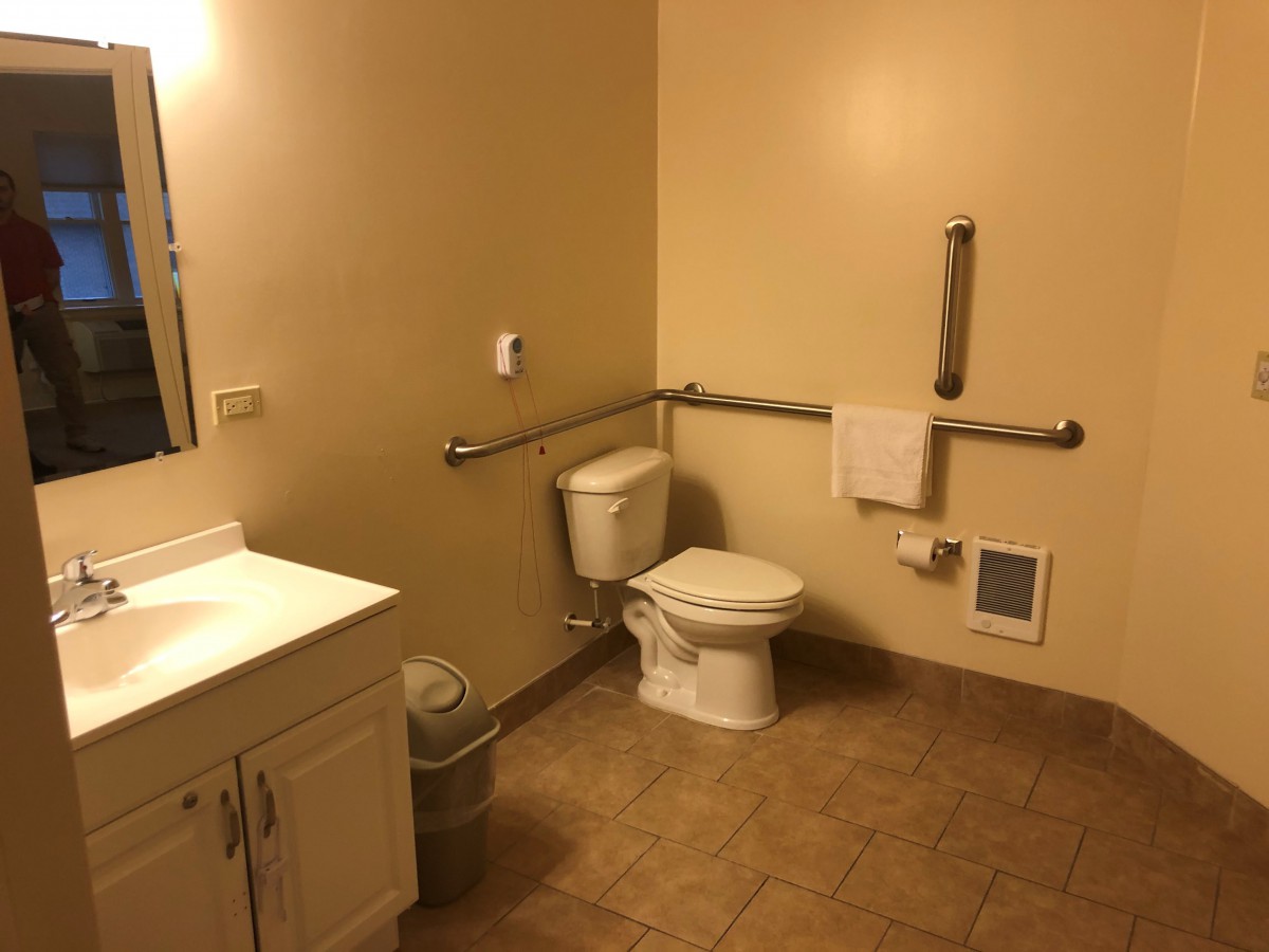 An accessible bathroom with a toilet, sink, and handrails.