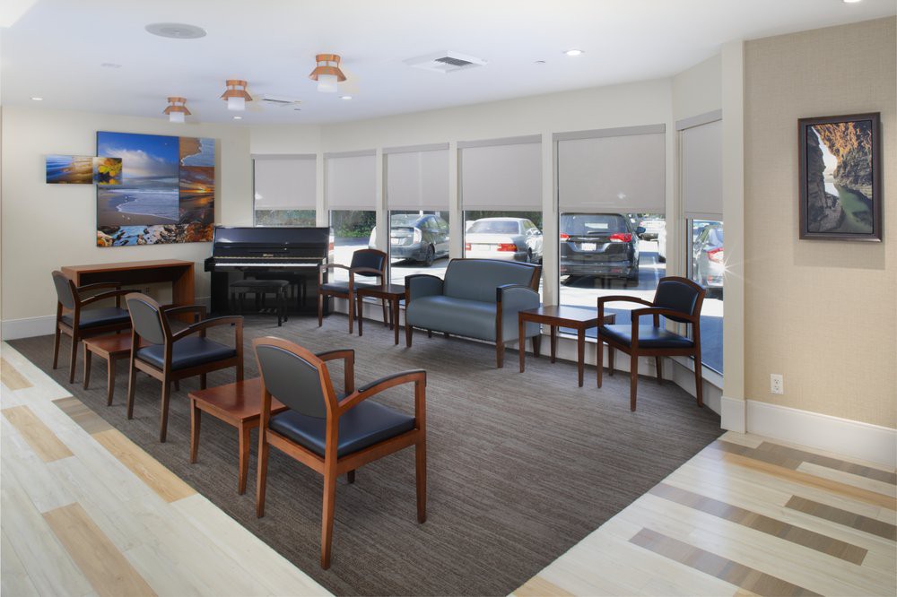 A spacious waiting room with several chairs, a piano, and large windows.