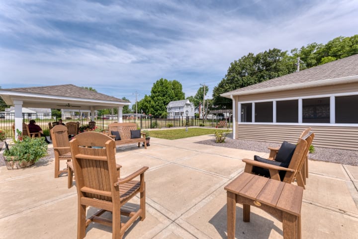 A spacious outdoor patio area with wooden furniture, surrounded by a garden on a sunny day.