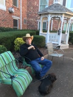 A man wearing a cowboy hat sits on a patio next to a gazebo.