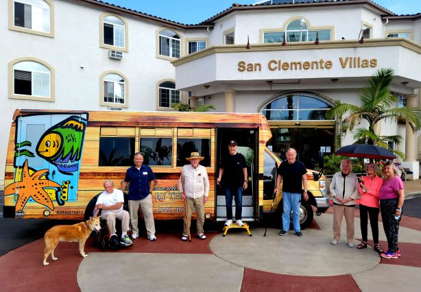 A group of people standing in front of a colorful bus near the San Clemente Villas entrance.