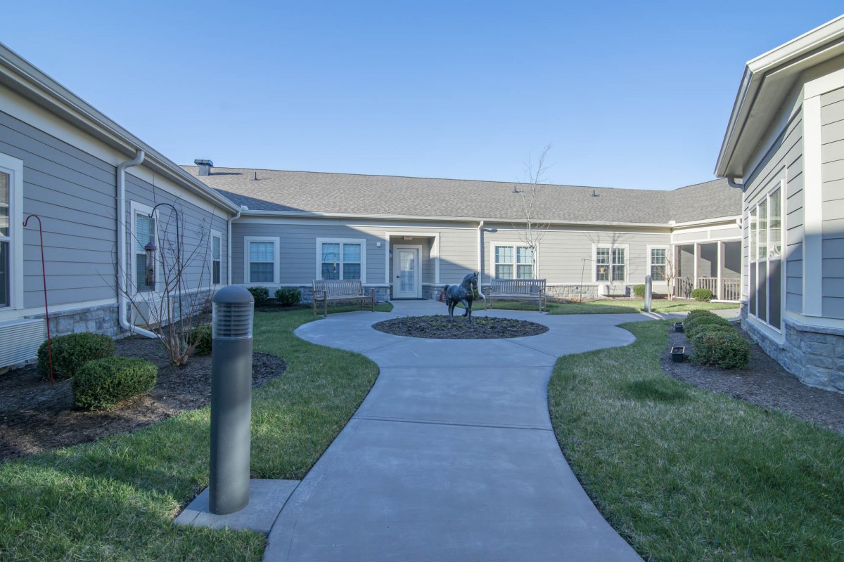 A serene courtyard with a pathway leading to a building, surrounded by well-maintained lawns and benches.