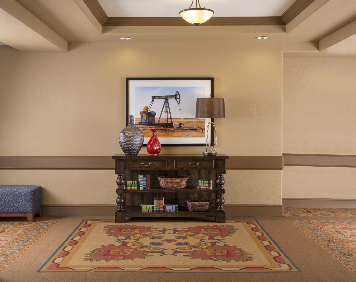 A decorated hallway with a table, vase, lamp, and painting above a patterned rug.