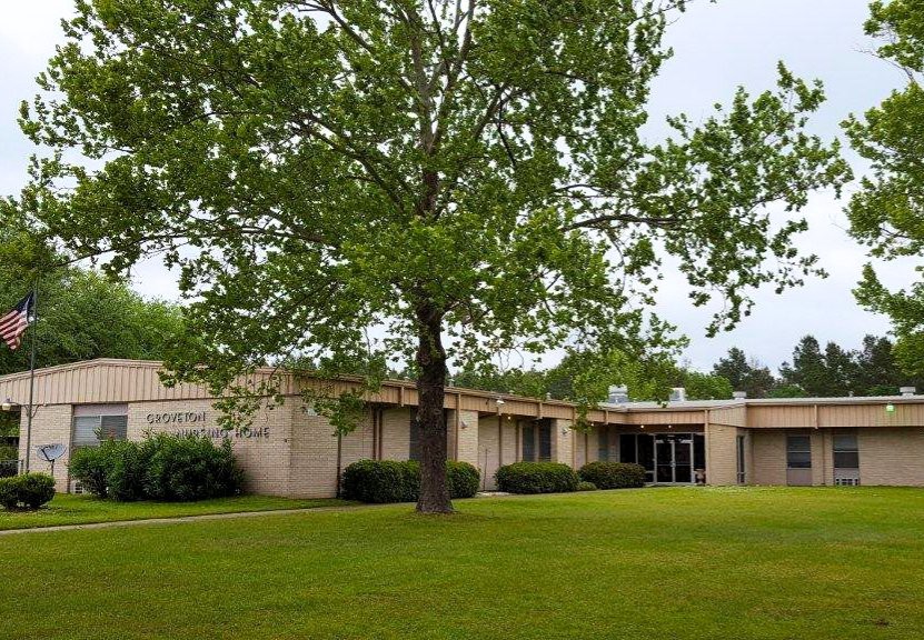 A view of a single-story building surrounded by a lush green lawn and trees.