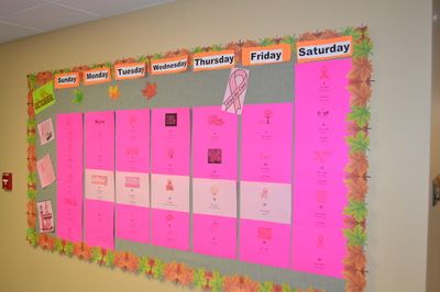 A colorful classroom bulletin board displays a weekly schedule with pink sections for each day of the week.