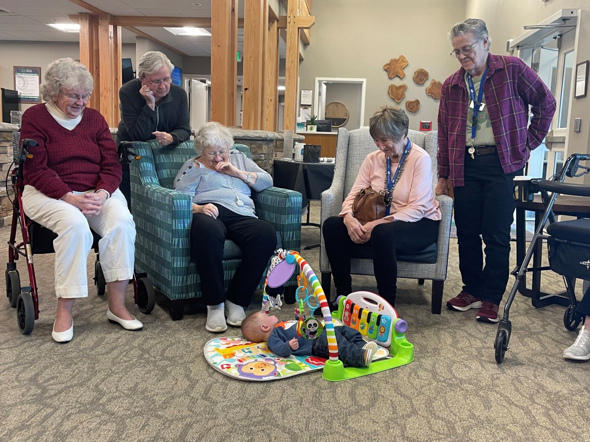 Seniors gather around a playmat, enjoying time with children in a community setting.