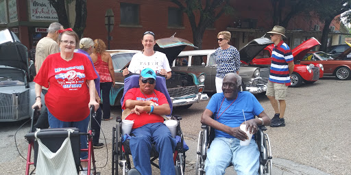 A lively outdoor community event showcasing classic cars, with attendees enjoying the day in wheelchairs.