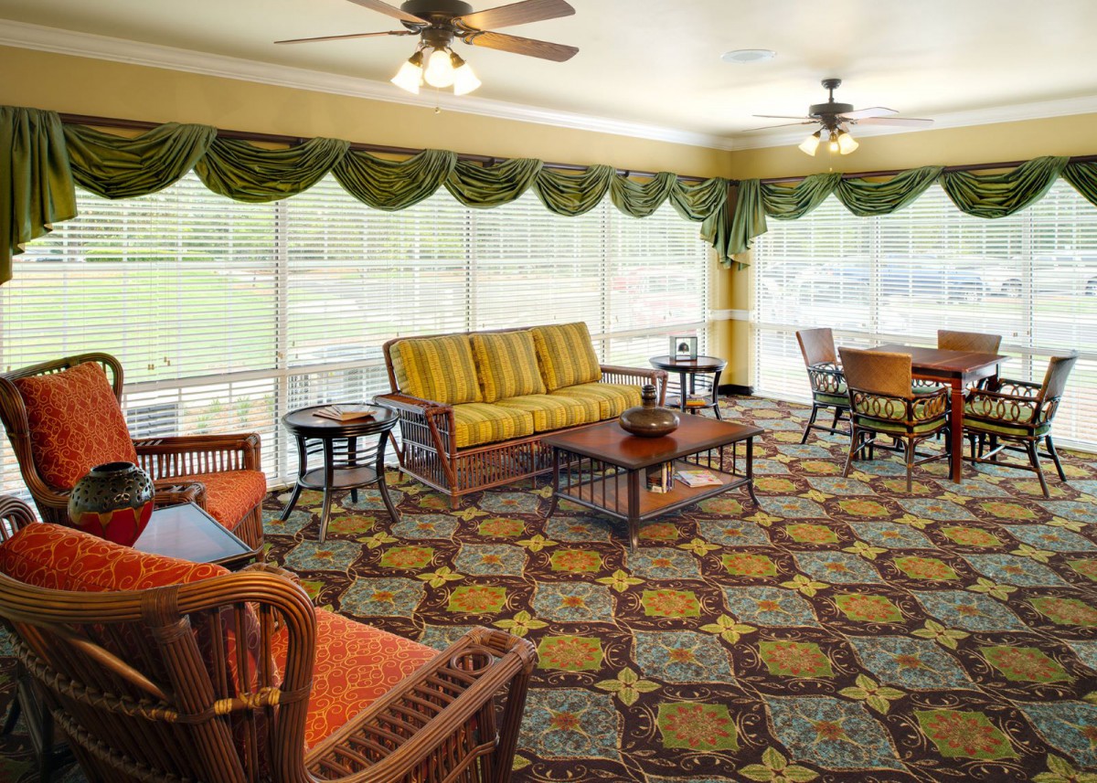 A cozy living room with patterned carpet, wicker furniture, and large windows.