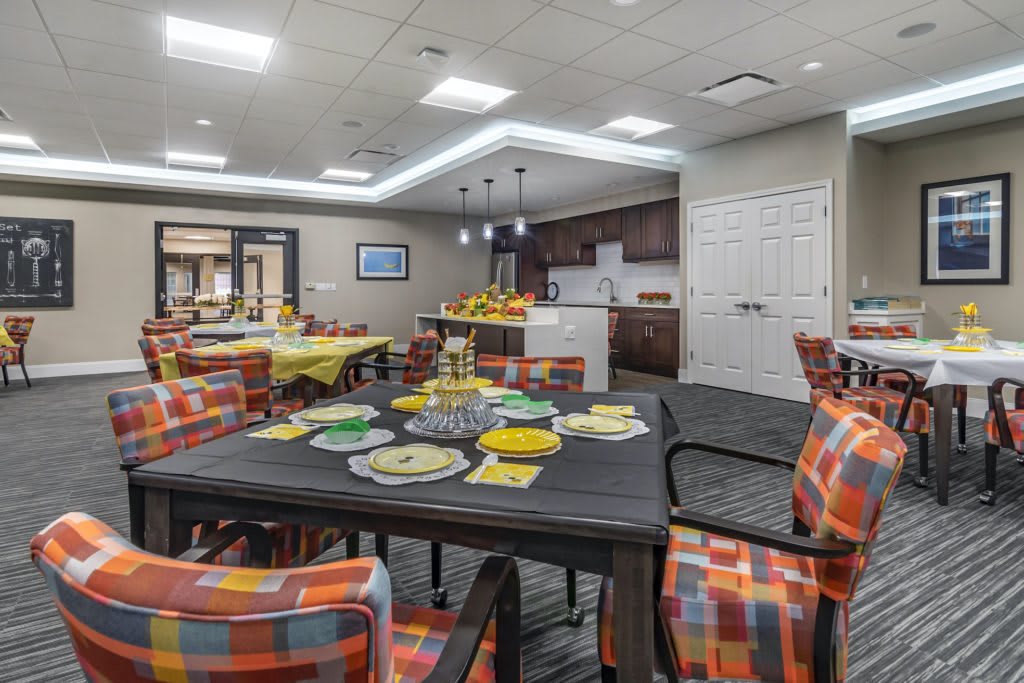 A modern dining area with decorated tables and vibrant chairs adjacent to a kitchen.