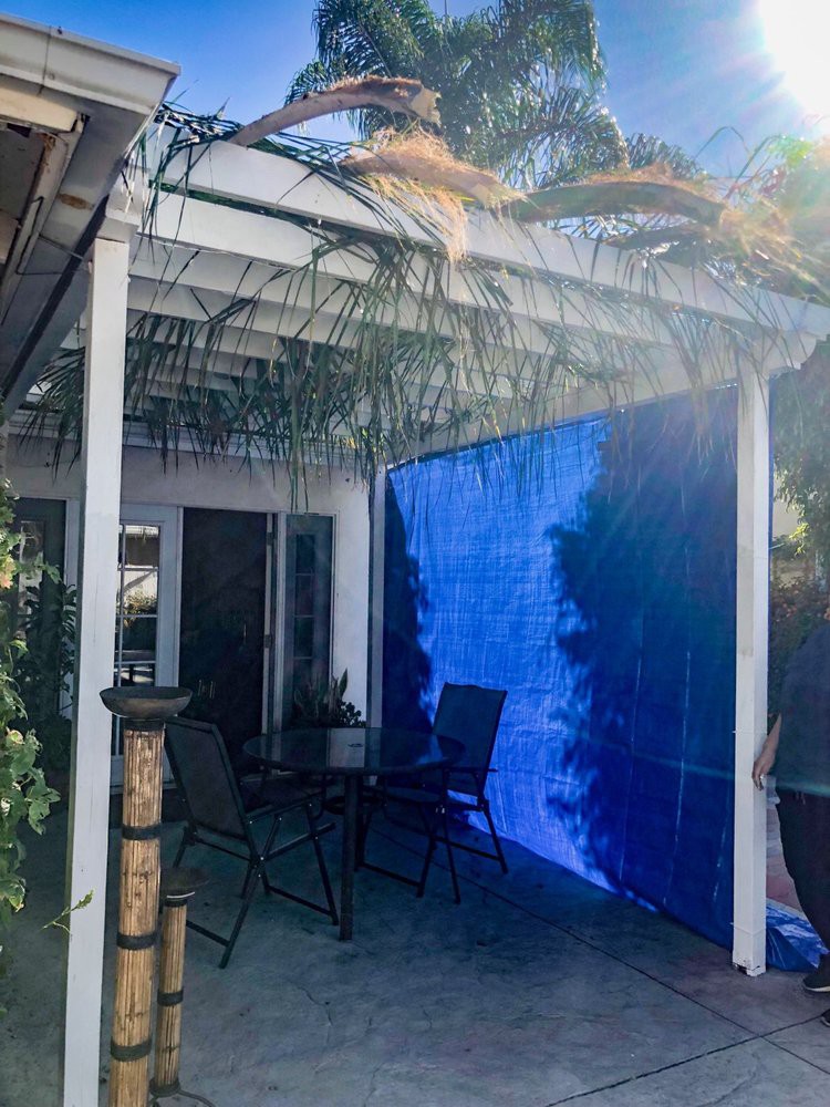 A backyard patio area with a pergola, featuring outdoor seating and a blue tarp for shade.