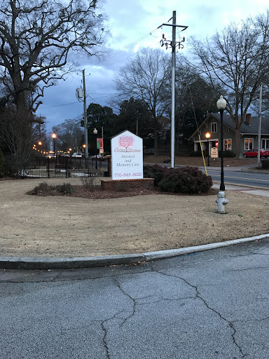 A park area with a sign illuminated in the evening light, surrounded by trees and street lamps.
