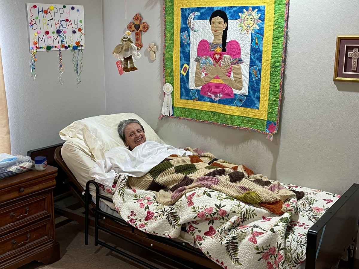 A person is lying in a bed with a colorful quilt on the wall and various room decorations.