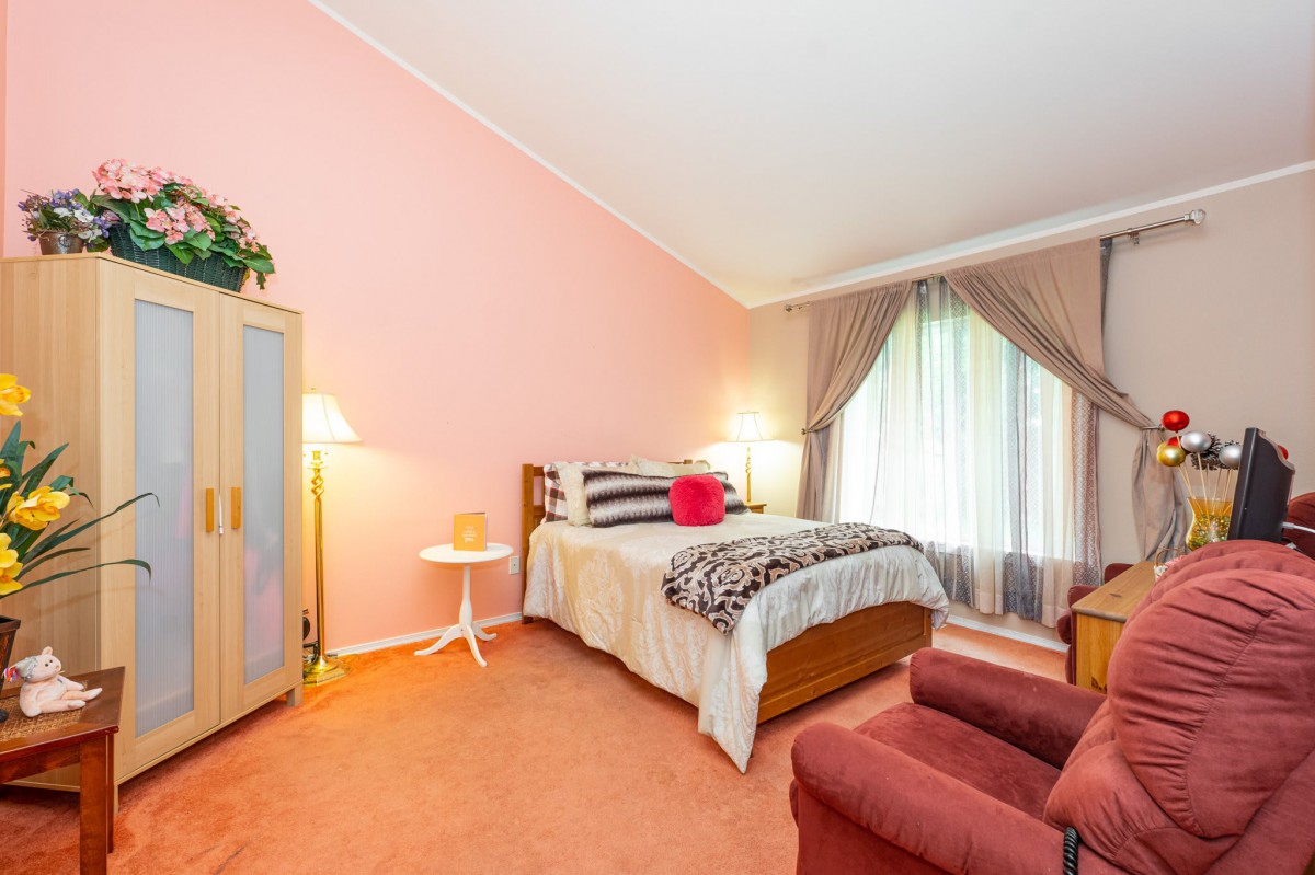 A cozy bedroom with pink walls, featuring a bed, armchair, and ample lighting.