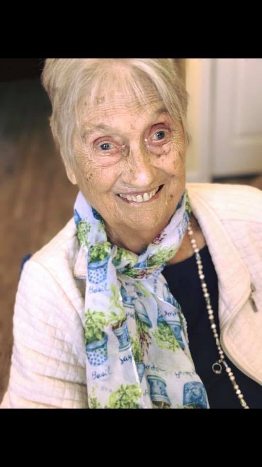 An elderly person smiling and wearing a colorful scarf indoors.