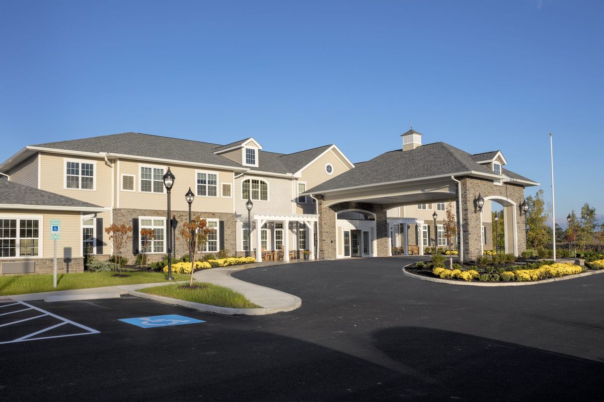 A large residential building with a landscaped entrance and driveway under a clear blue sky.