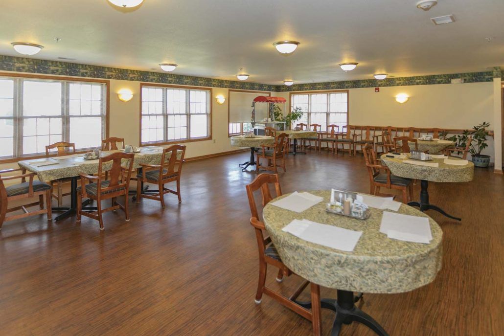 A spacious dining room with wooden floors, neatly arranged tables and chairs, and ample lighting.