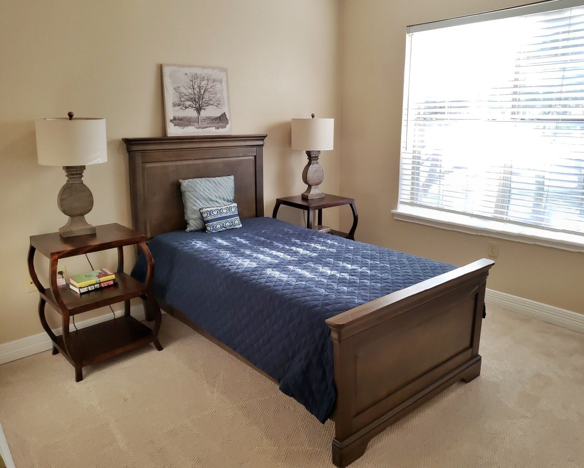A cozy bedroom with a neatly made bed, two nightstands with lamps, and a window letting in natural light.