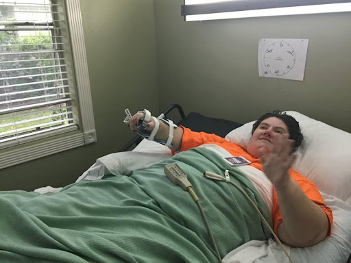 A patient lying in a hospital bed, recovering and waving.