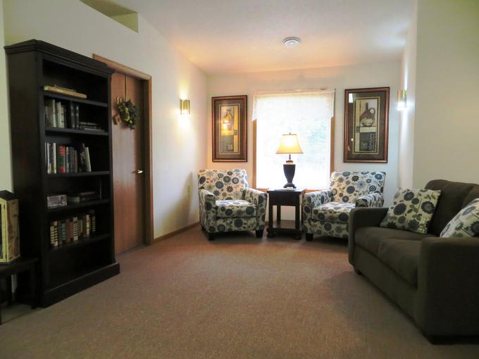 A cozy living room with two patterned chairs, a lamp, and a bookshelf.