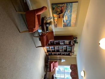 A cozy living room with a bookshelf, chairs, a sofa, and vibrant artwork.
