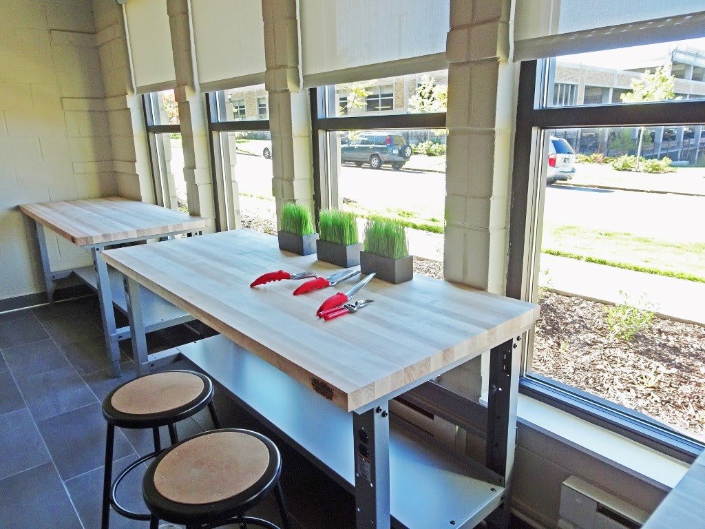 A bright cafe interior with a table, stools, and decorative plants by the windows.
