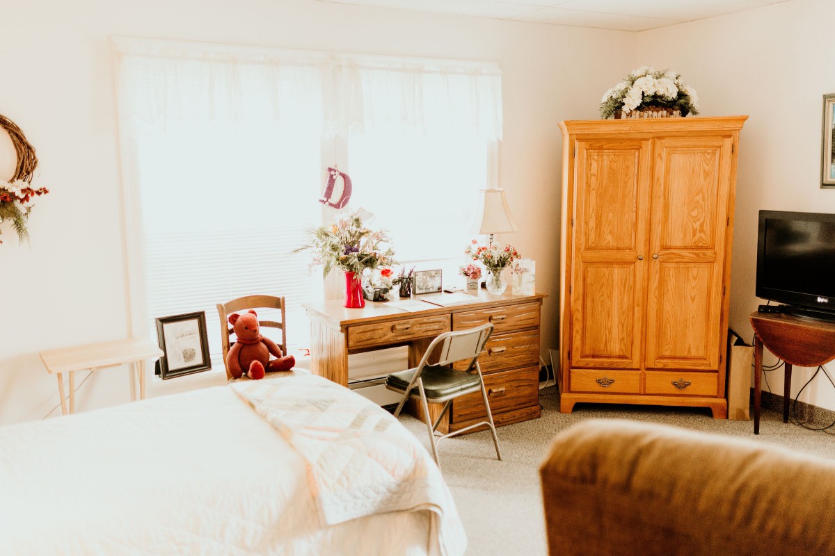 A cozy bedroom with warm wooden furniture, a comfortable bed, and natural light streaming in through the window.
