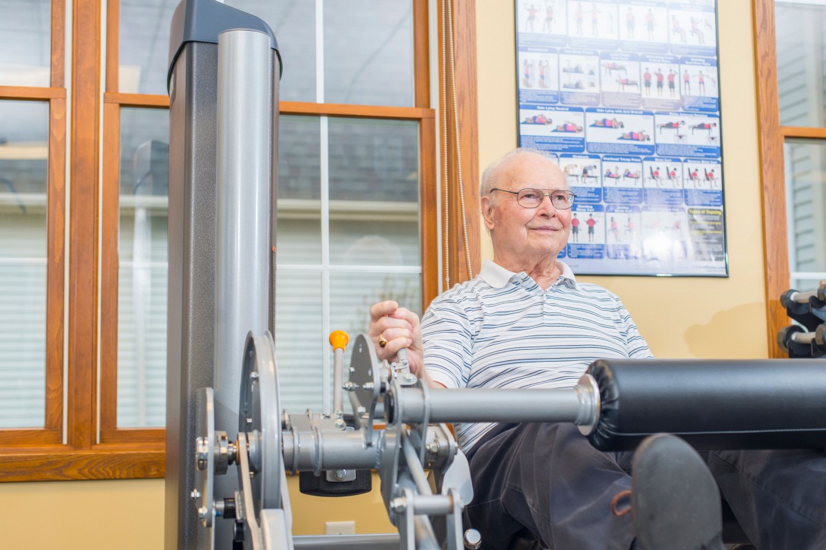 An elderly man using fitness equipment for exercise indoors.