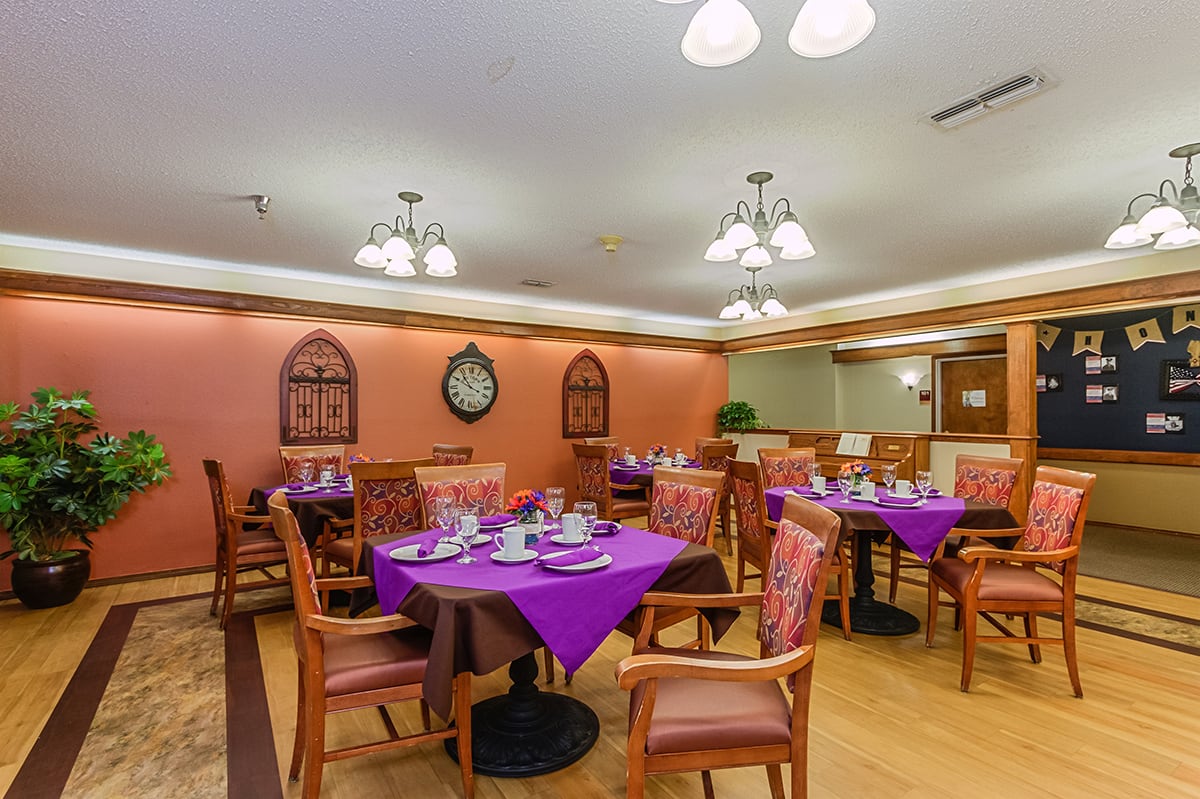 A cozy restaurant dining room with tables set with purple tablecloths and wooden chairs, illuminated by warm indoor lighting.
