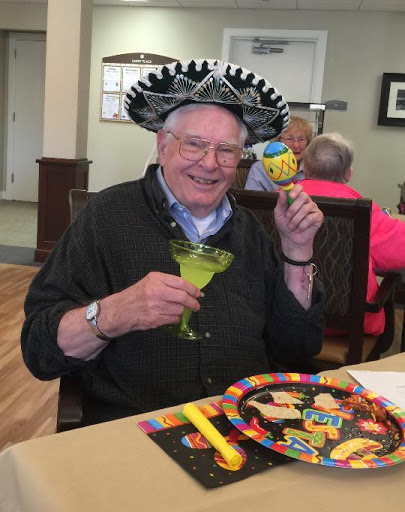 An elderly man enjoying a festive celebration with a colorful hat and a refreshing drink.