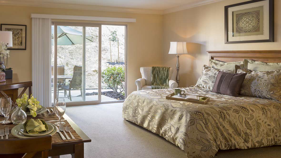 A cozy bedroom with a view of a sunny patio through sliding glass doors.