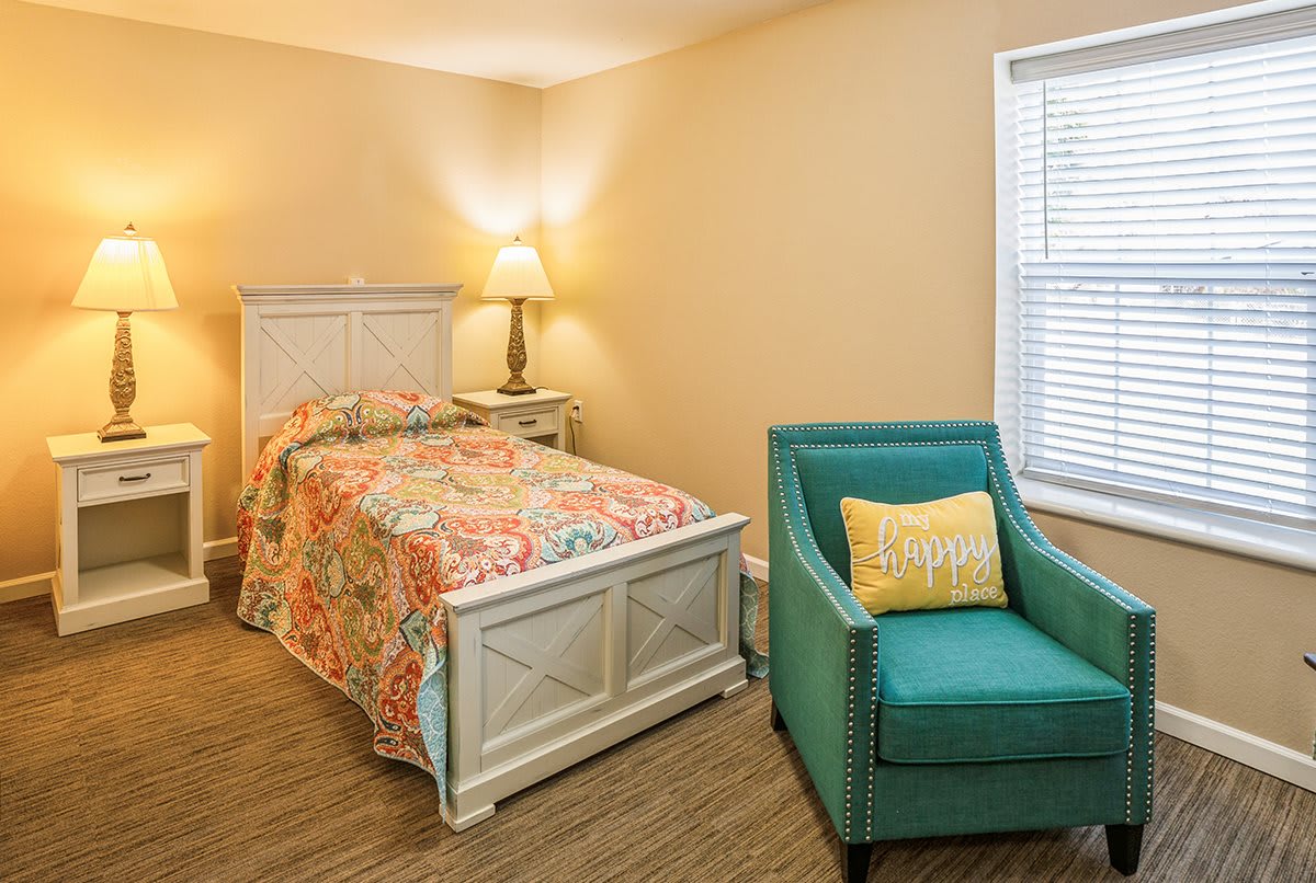 A cozy bedroom with a single bed, an armchair, and warm lighting.