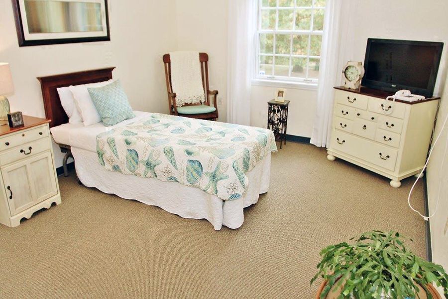 A cozy bedroom with a single bed adorned with floral bedding, a dresser, and a window letting in natural light.