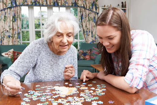 A heartwarming moment between a young woman and an elderly lady as they work together on a jigsaw puzzle.