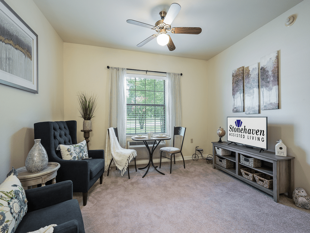 A cozy living room with a small table and chairs set, comfortable seating, a TV stand, and a ceiling fan.