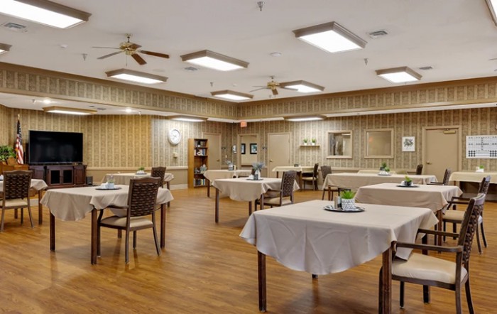 An empty dining room with neatly arranged tables and chairs, featuring wood flooring and elegant lighting.