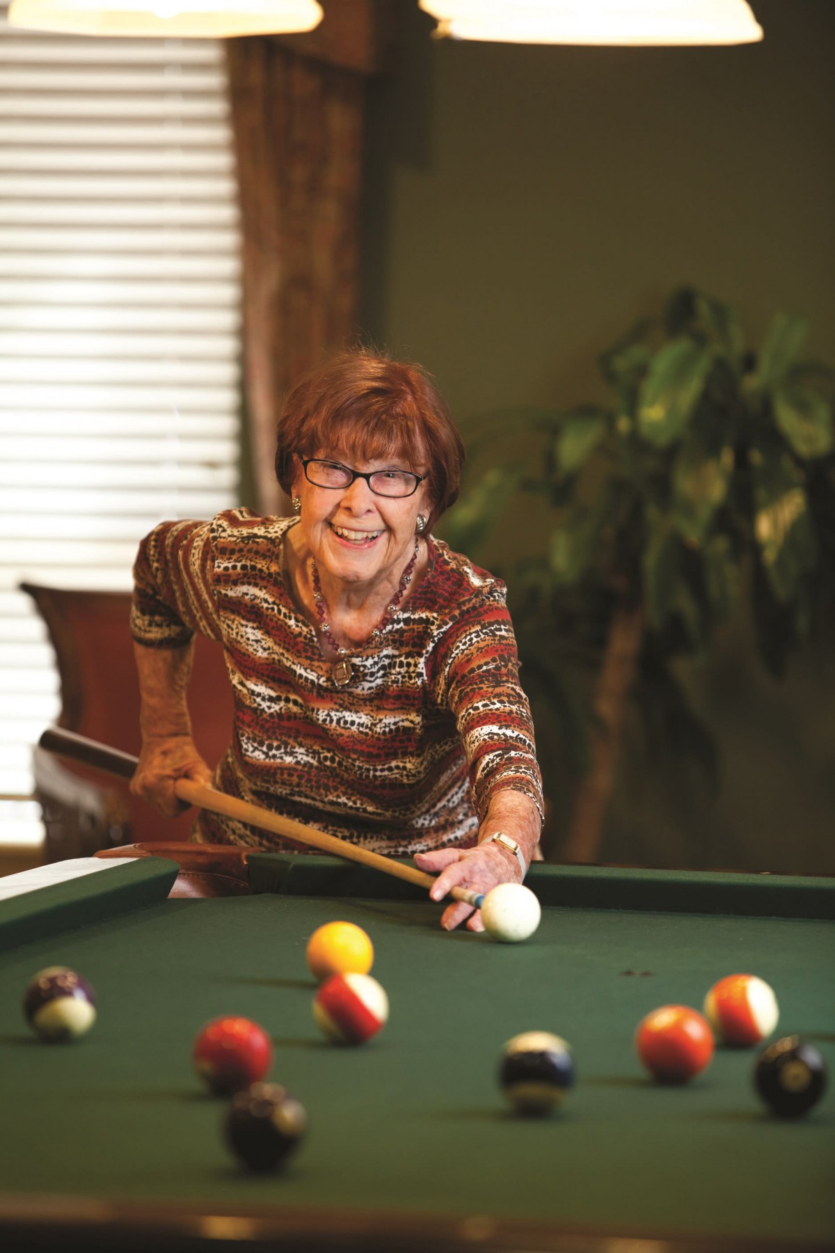 An elderly woman playing pool indoors with a focused expression.