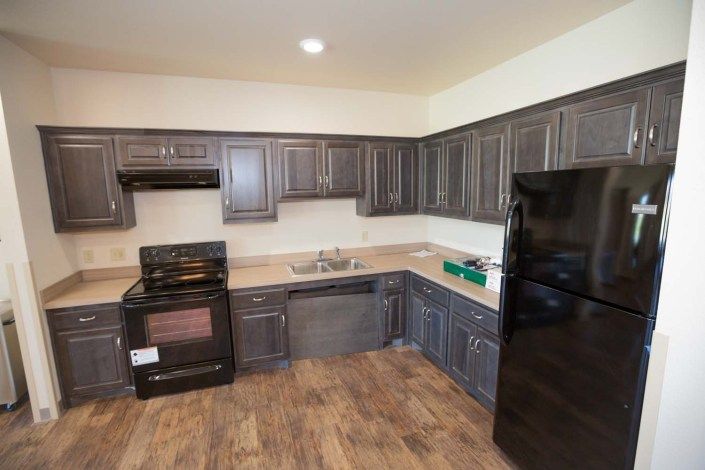 A modern kitchen with dark cabinets, appliances, and wooden flooring.