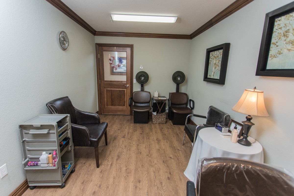 A small waiting area in a hair salon with chairs, magazines, and hair drying equipment.