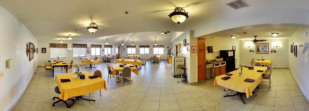A spacious dining room with neatly arranged tables and chairs, featuring large windows and warm lighting.