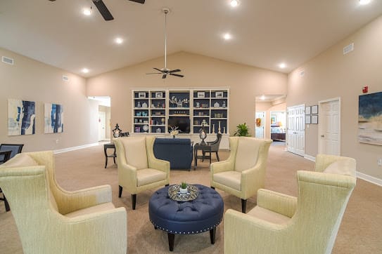 A well-decorated living room with modern furniture, including yellow armchairs, a blue ottoman, and built-in bookshelves.