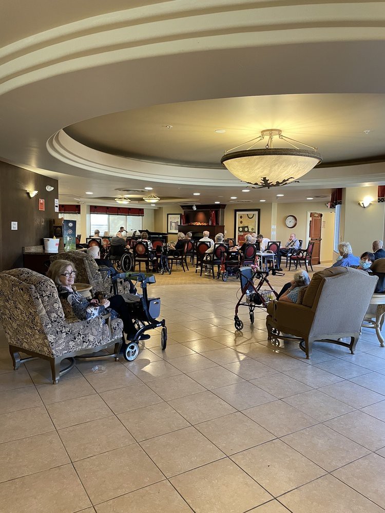 A spacious lobby with several people seated, featuring comfortable chairs and a central chandelier.