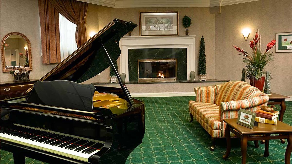 A cozy living room featuring a grand piano, a fireplace, and a striped sofa on a green carpet.