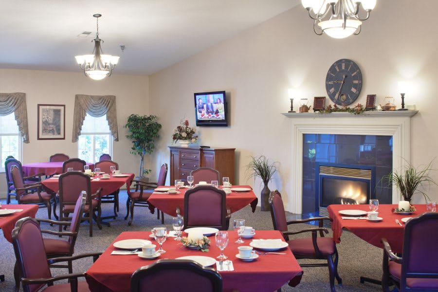 A cozy dining room with elegant table settings, a fireplace, and chandeliers.