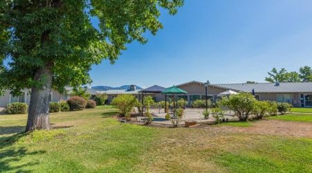 A scenic outdoor garden area with a patio under a clear blue sky, surrounded by lush greenery.